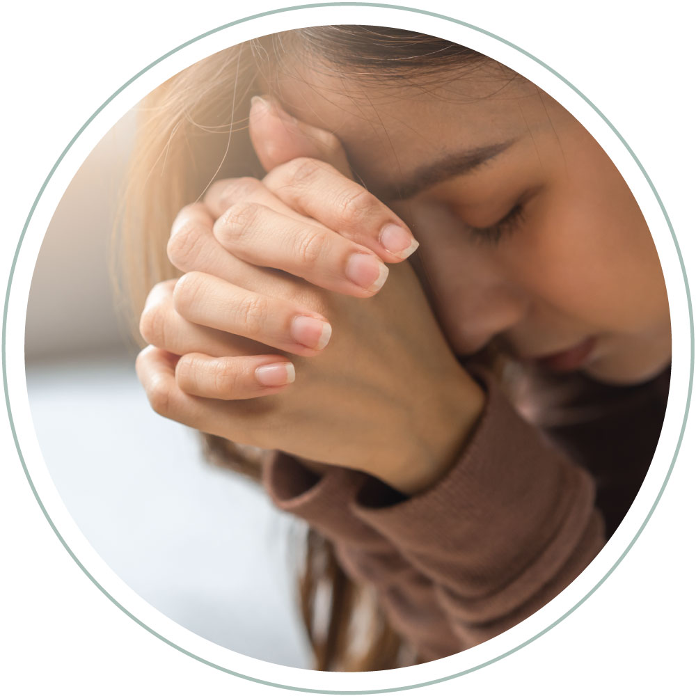 a woman seeking divine intervention with her eyes closed leaning into her clasped hands as she prays