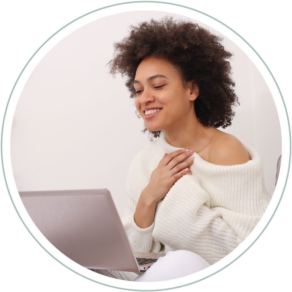 a woman holding her heart with a smile while on her computer having an online Catholic Psychotherapy session
